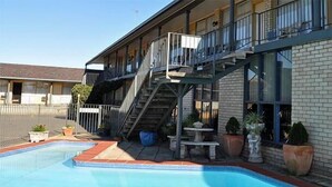 A hotel with a swimming pool, outdoor seating, and a staircase leading to the upper floor. - Adrian Motel (Forbes)