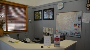A reception desk with a sign instructing to ring the bell for service, a clock, framed pictures, a map, and a bulletin board with various notices. - Adrian Motel (Forbes)