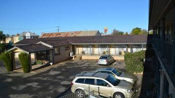 A motel with a parking lot, a small covered area, and a building with a tiled roof.
