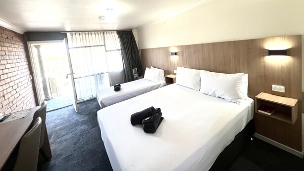 A hotel room with two beds, a desk, a chair, a small table, and a nightstand. - Adrian Motel (Forbes)