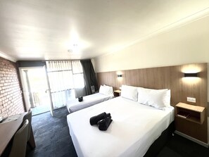 A hotel room with two beds, a desk, a chair, a small table, and a nightstand.