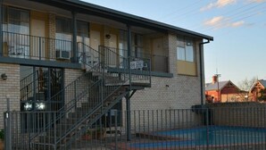 A two-story brick building with a sign reading "RESTAURANT" above the entrance. There is a staircase leading to the upper floor, and a fenced outdoor area with a pool. - Adrian Motel (Forbes)