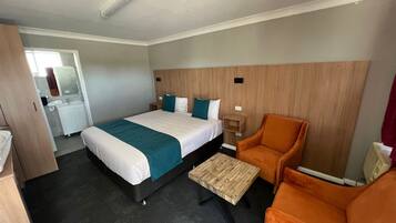 A hotel room with a bed, a wooden nightstand, an orange armchair, a small wooden table, and a mirror.