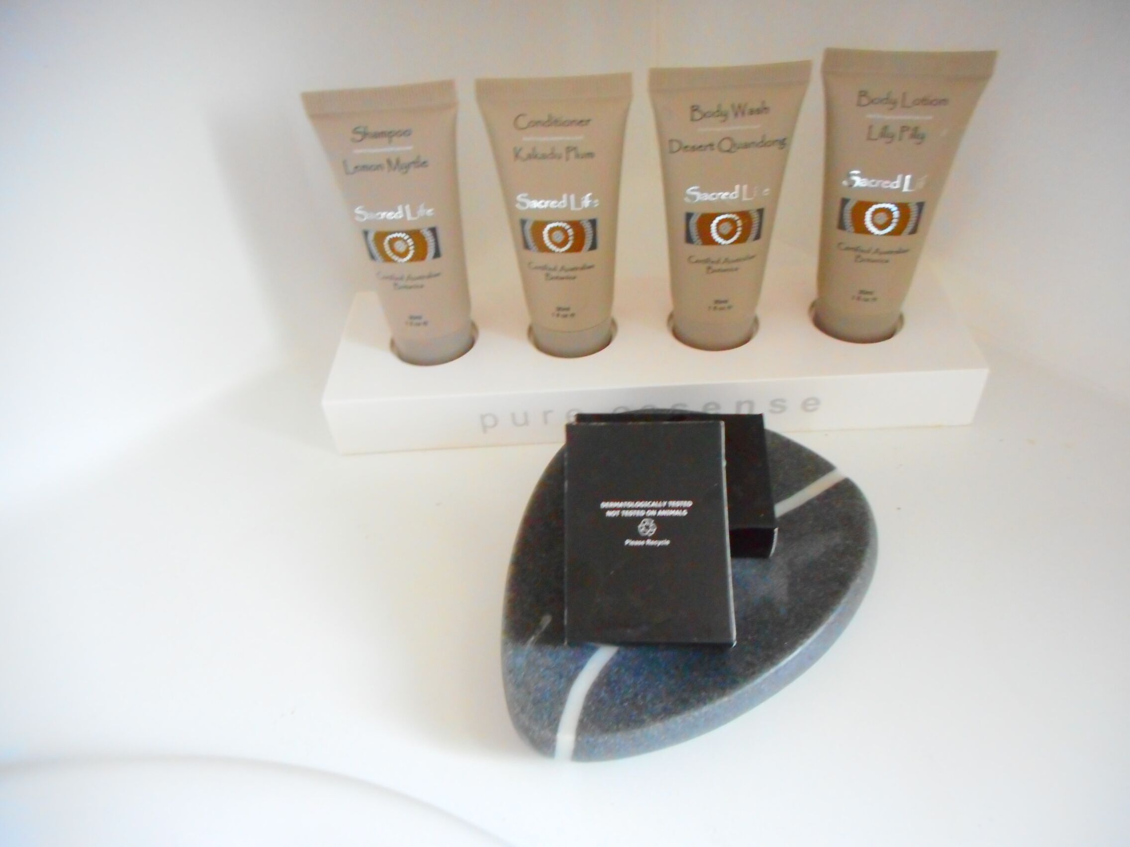 A display of four body care products on a white shelf with a black box below.