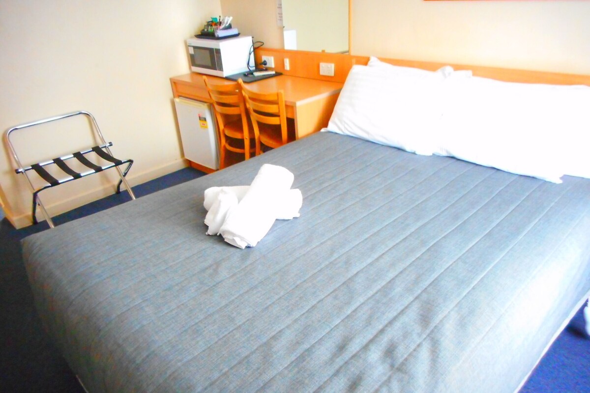 A hotel room with a bed, a desk with a microwave, a chair, and a small refrigerator.