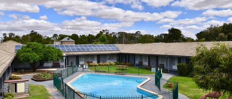 A swimming pool surrounded by a green fence, with a building in the background and a clear sky.