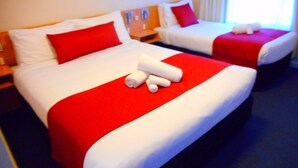 Et hotelværelse med to senge, begge med hvidt og rødt sengetøj, og et rødt tæppe på den ene seng.