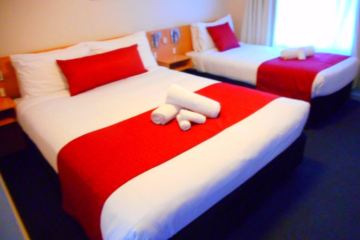 Une chambre d’hôtel avec deux lits, chacun recouvert d’une literie blanche et rouge, et un plaid rouge sur l’un des lits.