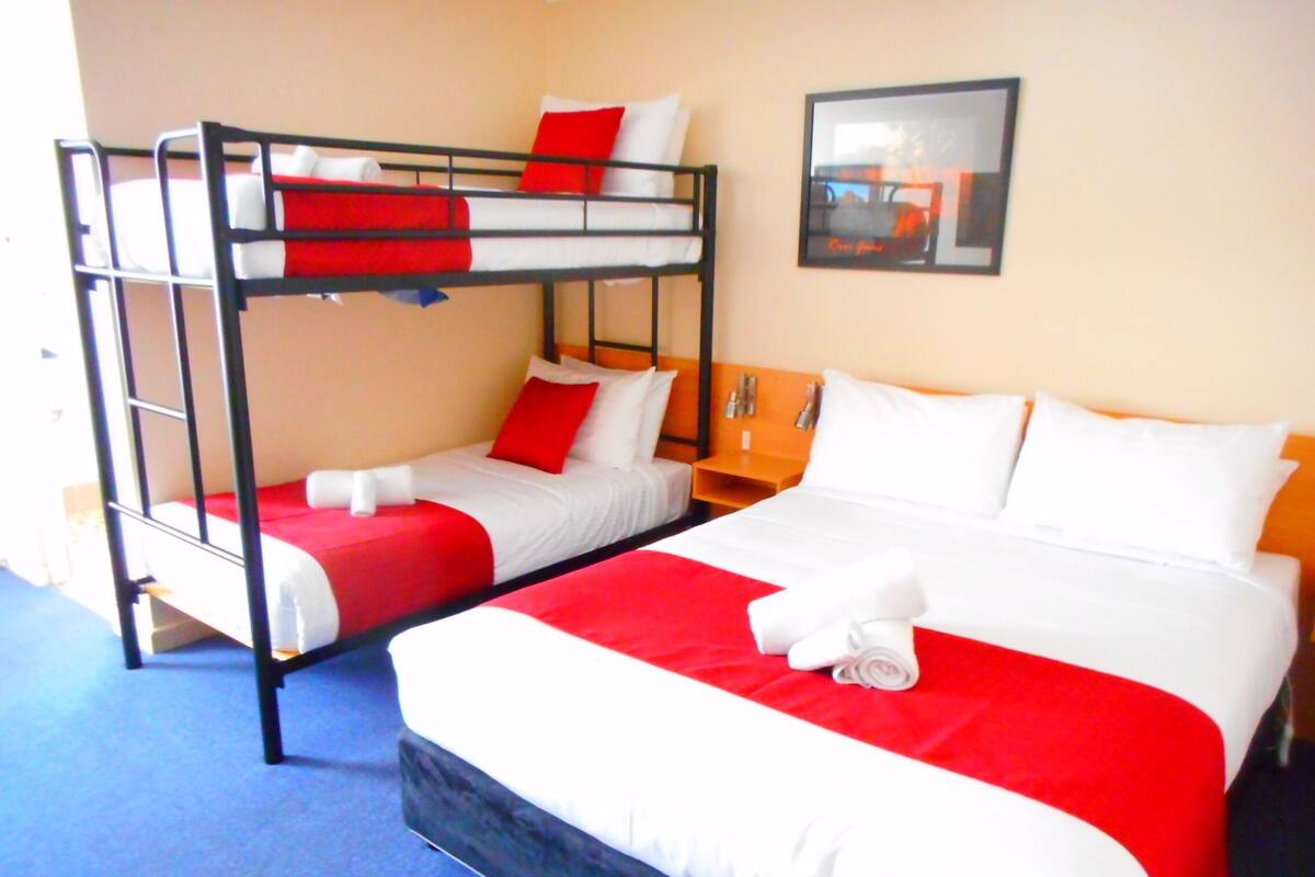 Une chambre d’hôtel avec un lit superposé et un lit simple, tous deux dotés de draps rouges et blancs.