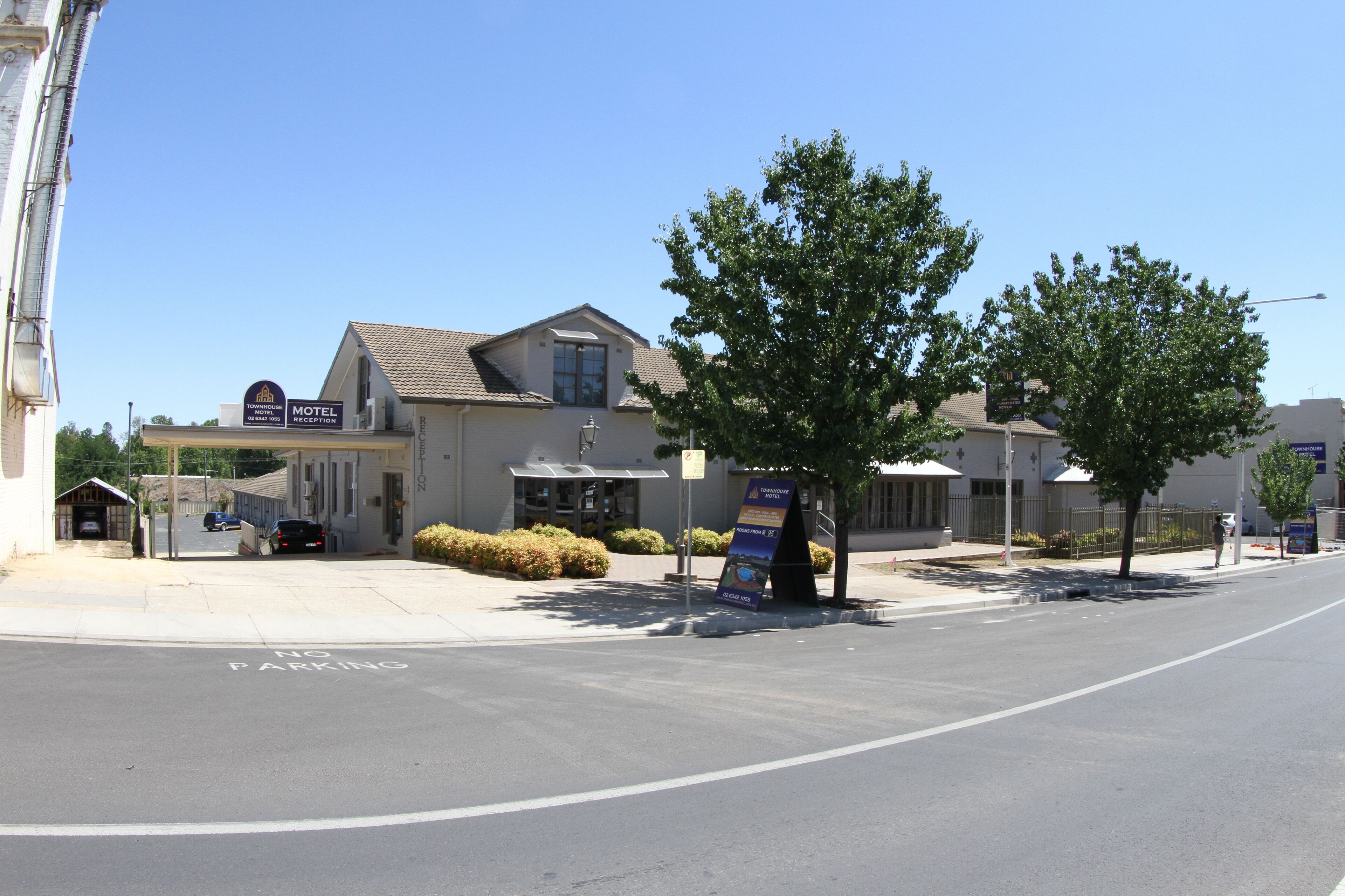 A motel with a reception area, a parking lot, and a tree-lined street.