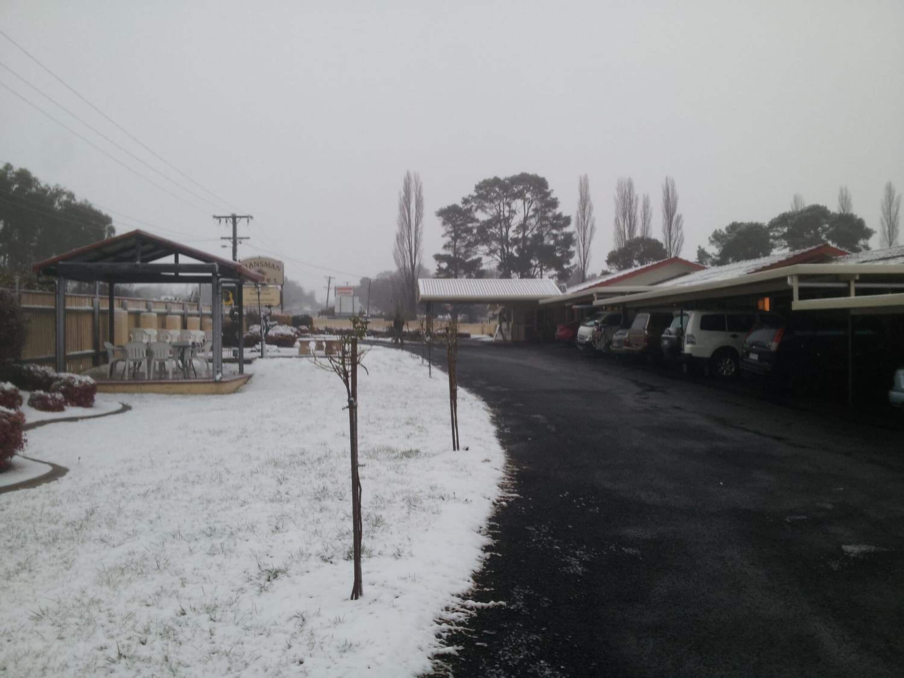 Un estacionamiento cubierto de nieve con un área de estar al aire libre techada y un edificio con un letrero.
