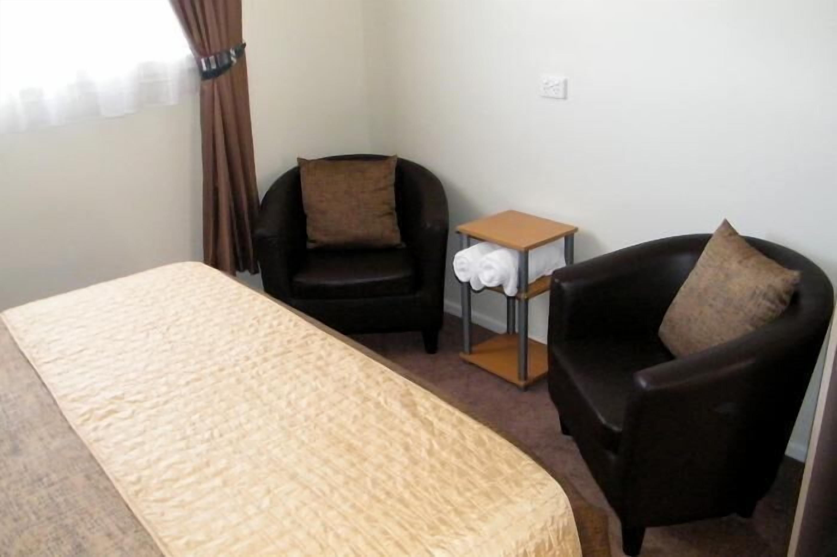 Una habitación con cama, dos sillones, una mesita con una toalla y una ventana con cortinas.