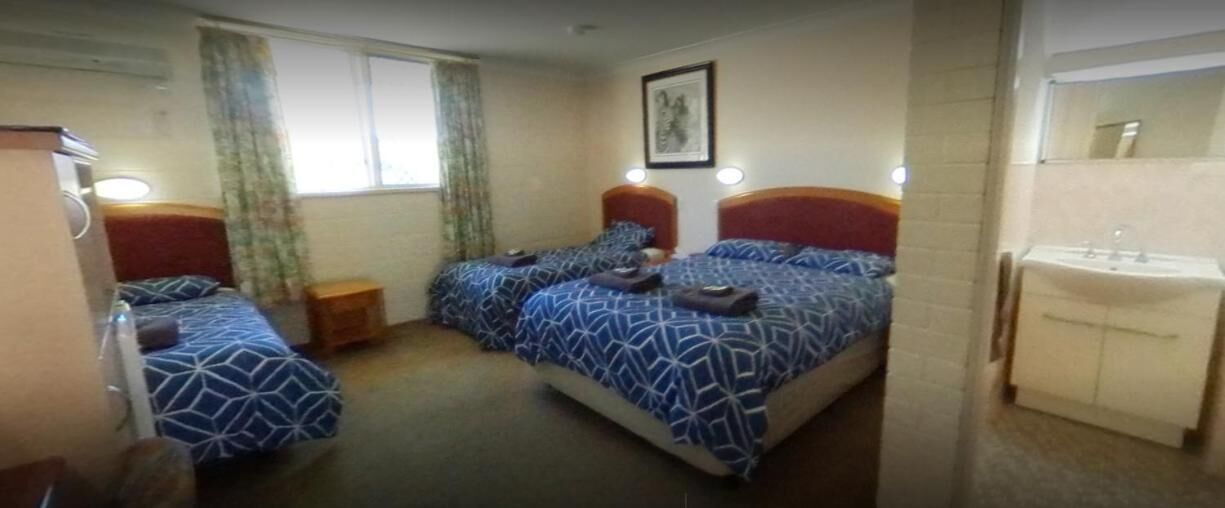 A hotel room with two beds, a small bedside table, a mirror, and a bathroom with a sink and toilet.