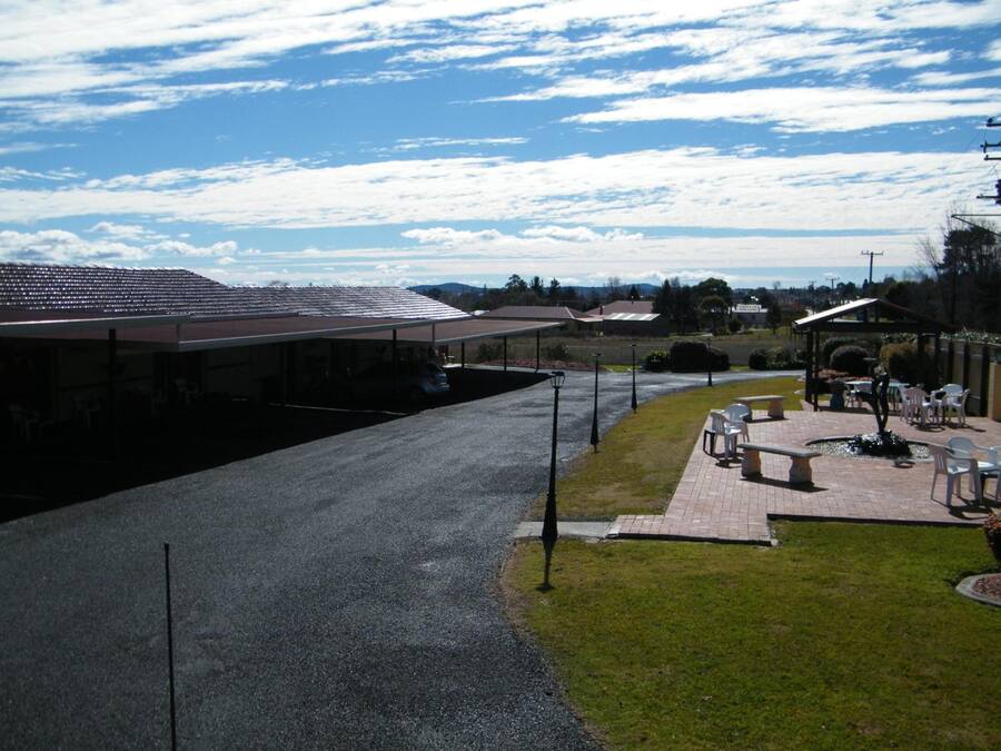 A parking lot with a covered area, a grassy area with outdoor seating, and a building with a sloped roof.
