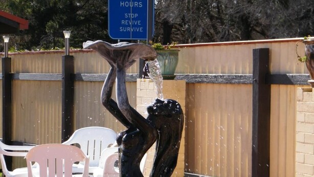 Eine Skulptur, die eine Person zeigt, die versucht, Wasser zu fangen, mit einem Schild im Hintergrund, auf dem steht: 'EVERY TWO HOURS STOP REVISE SURVIVE'.