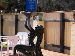 A sculpture of a person reaching up to catch water, with a sign in the background that reads "EVERY TWO HOURS STOP REVISE SURVIVE." - The Clansman Motel (Glen Innes)