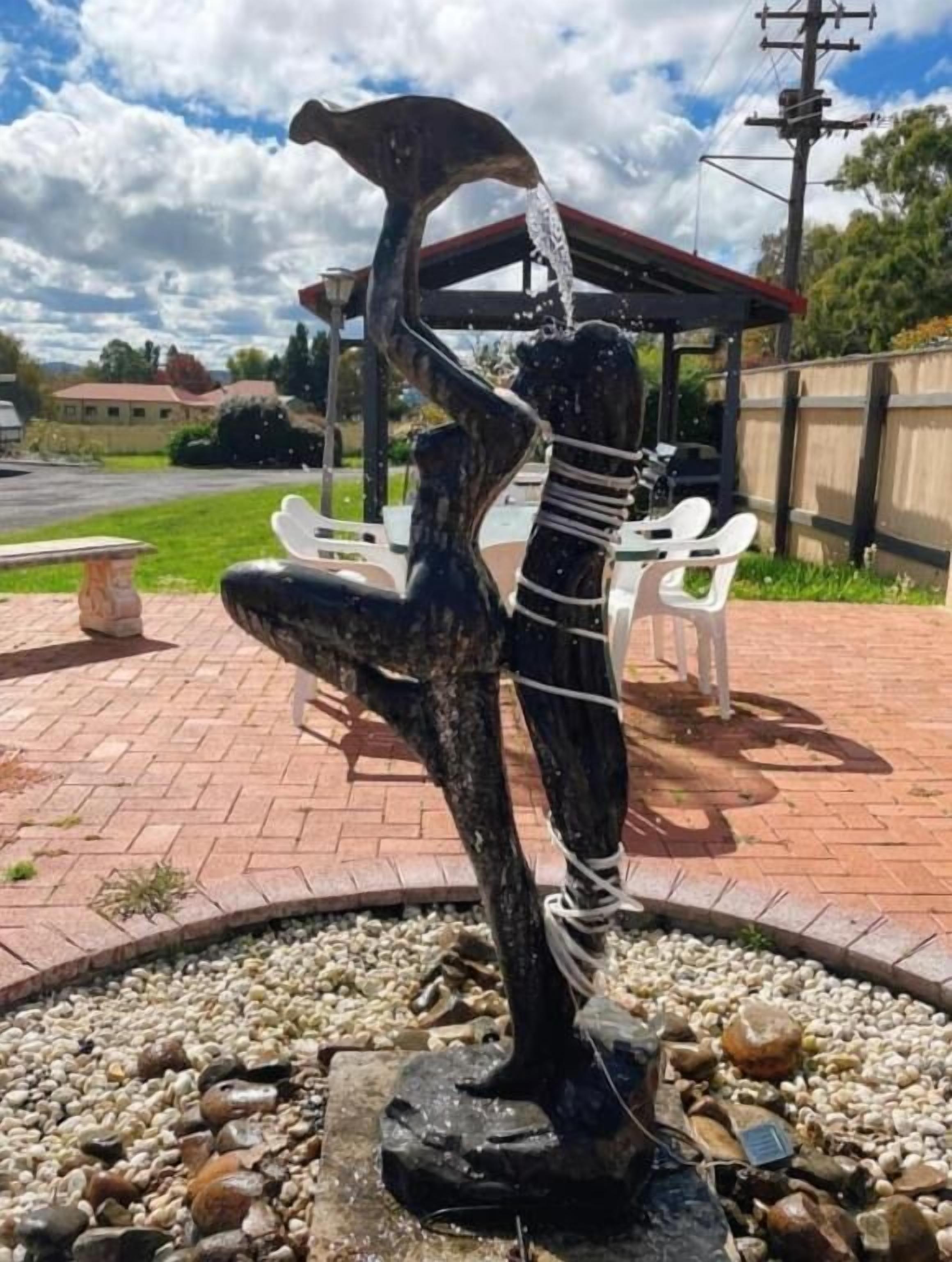 Une sculpture représentant une figure tenant une coupe, entourée d’une bordure circulaire en pierre, avec un espace de repos abrité en arrière-plan.