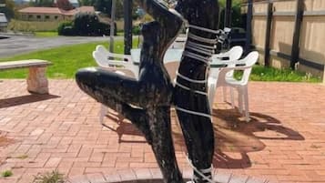 Une sculpture représentant une figure tenant une coupe, entourée d’une bordure circulaire en pierre, avec un espace de repos abrité en arrière-plan.