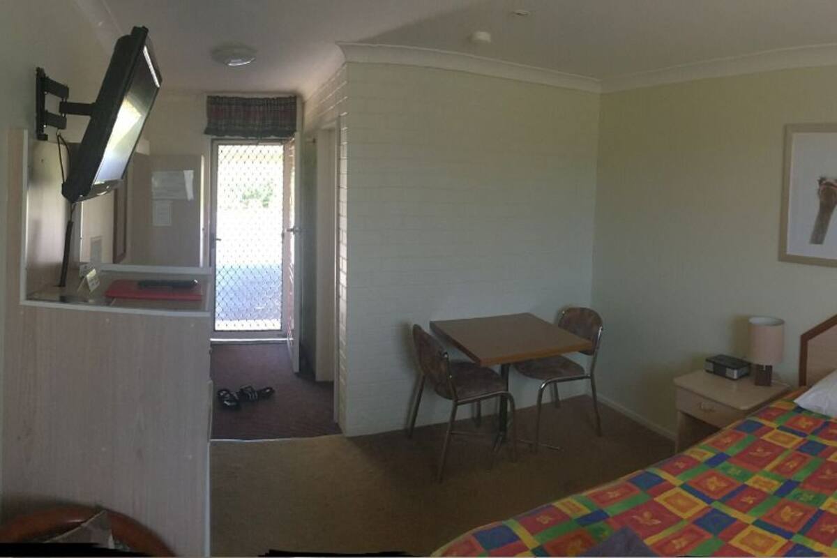 A hotel room with a bed, a desk, a chair, a nightstand, and a window.