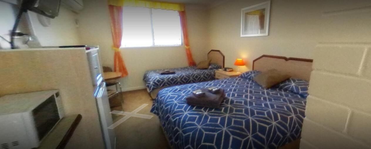 Una habitación con dos camas, un escritorio, una silla, una lámpara y una ventana con cortinas.