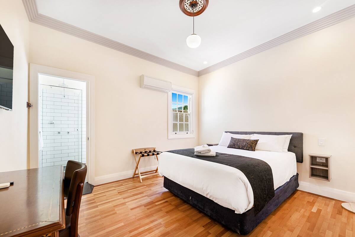 A bedroom with a bed, a desk, a chair, a window, and a door.