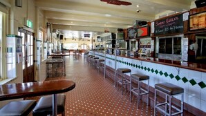A restaurant with a bar area, multiple seating options including bar stools and tables, and a tiled floor. - Canungra Hotel (Canungra)