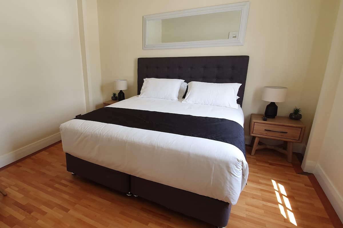 A bedroom with a large bed, two bedside tables with lamps, a small plant, and a chair.