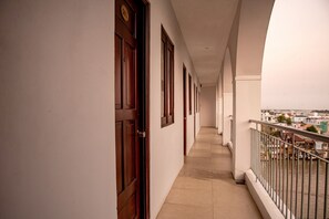 A corridor with doors, a balcony with a railing, and a view of buildings across a body of water. - Song Tien Annex Hotel (My Tho)