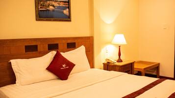 Quarto de hotel com uma cama bem arrumada, cabeceira de madeira, mesa de cabeceira com abajur e um quadro na parede.