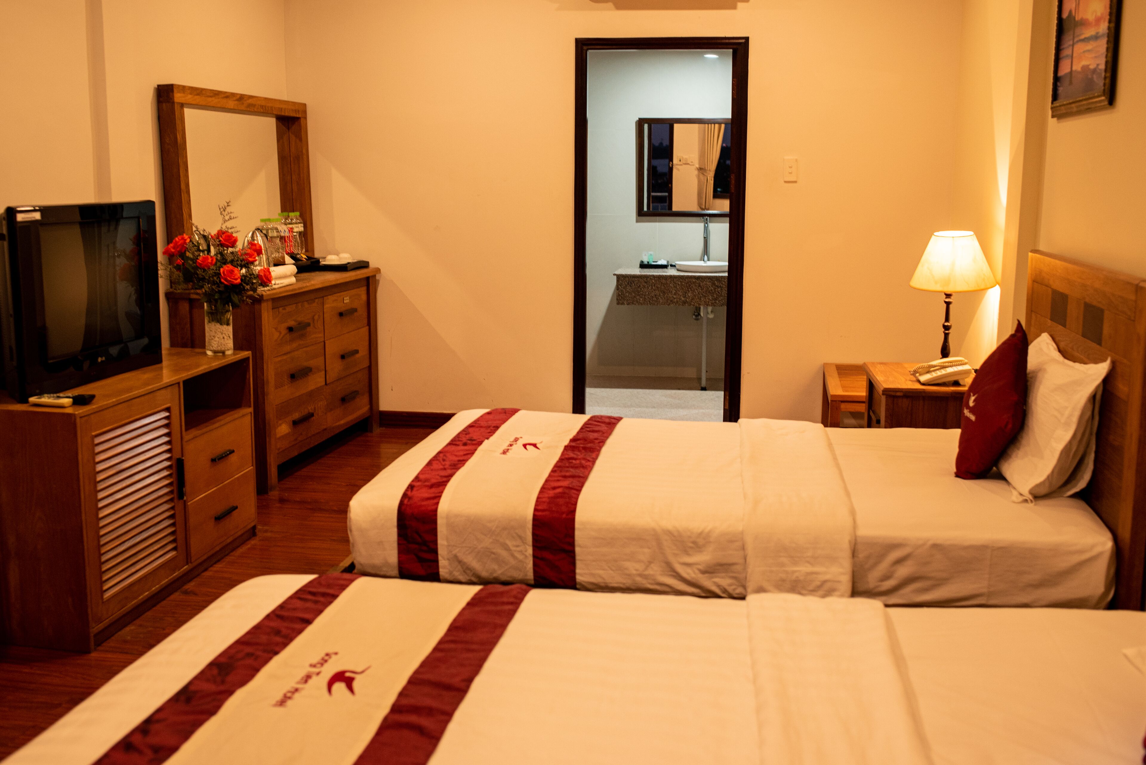 A hotel room with two beds, a TV, a dresser, and a bathroom visible through an open door.