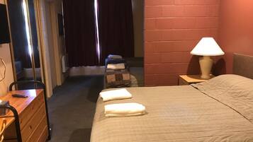 Une chambre d’hôtel avec un lit, un bureau, une chaise, une lampe et une fenêtre avec des rideaux.