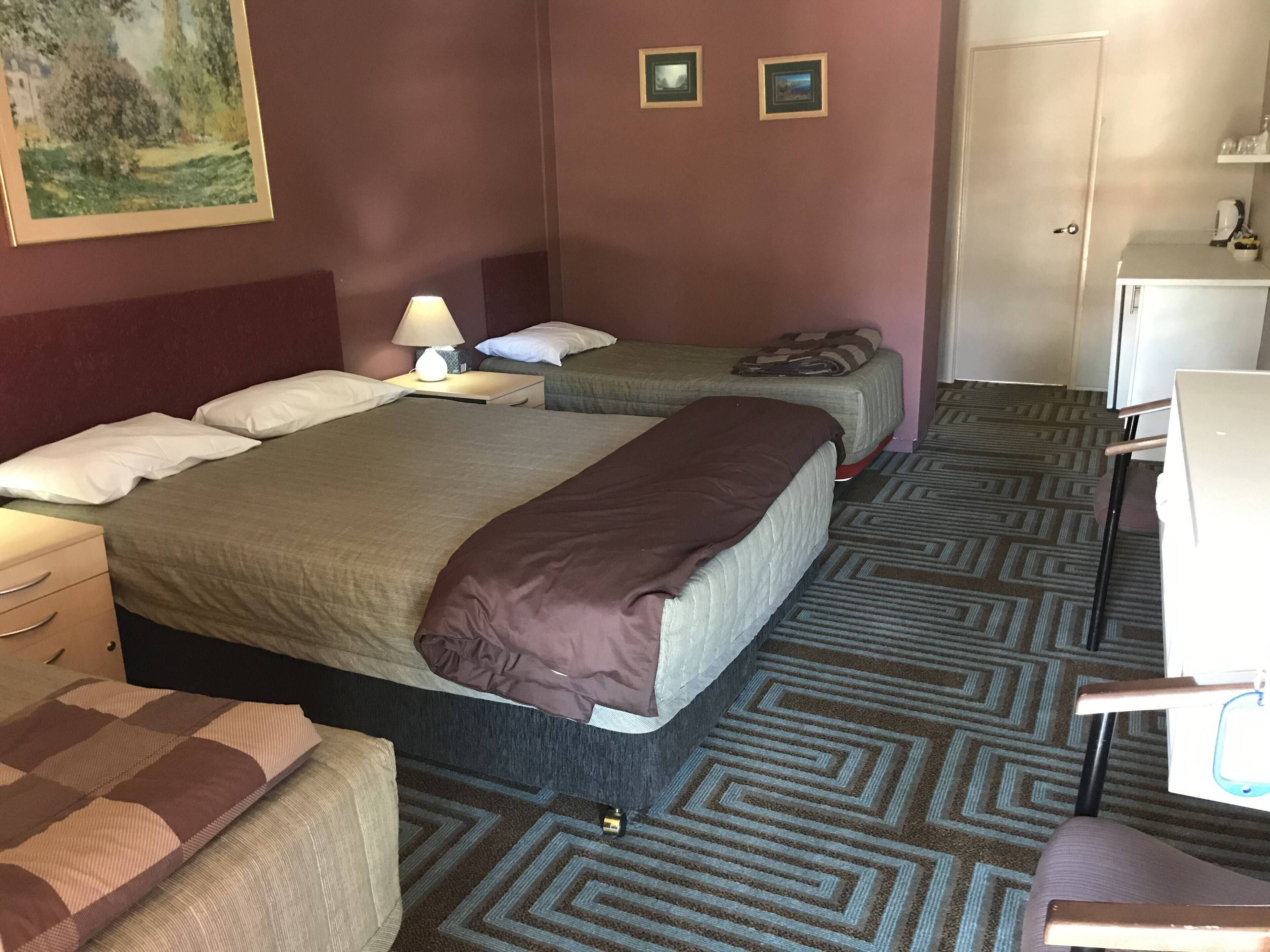 Une chambre d’hôtel avec deux lits, un bureau, une chaise, une lampe et un tableau au mur.