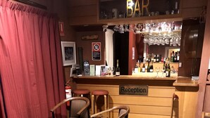 Zona de bar con mostrador de recepción, taburetes de bar y un perro sentado sobre una alfombra estampada.