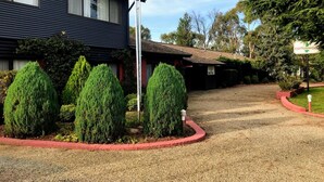 Un motel con camino de grava, arbustos de hoja perenne bien cuidados y bordillo rojo.
