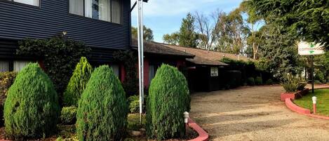 A motel with a gravel driveway, neatly trimmed evergreen shrubs, and a red curb.