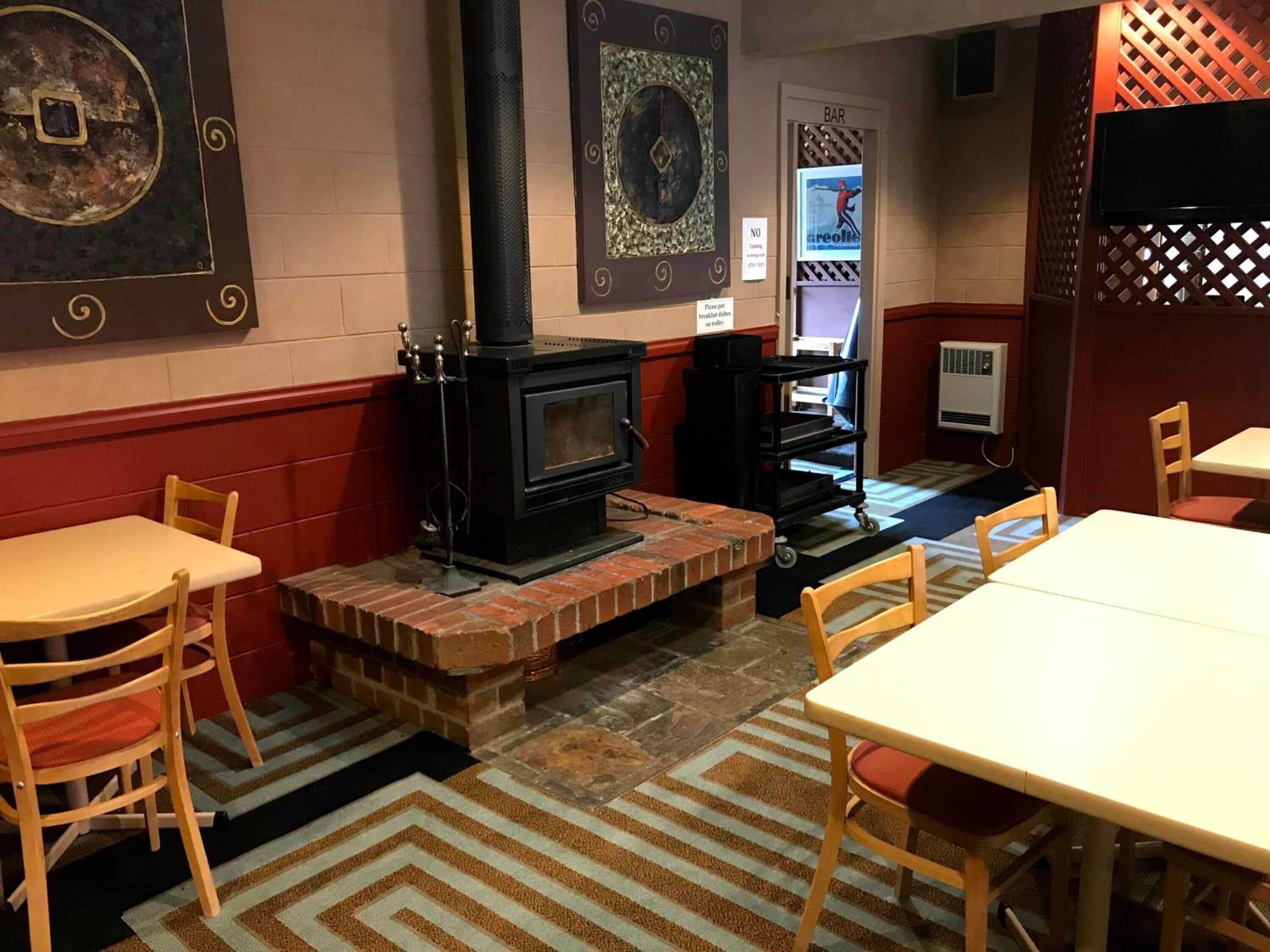A cozy room with a brick fireplace, wooden chairs, a white table, and a bar area with a TV.