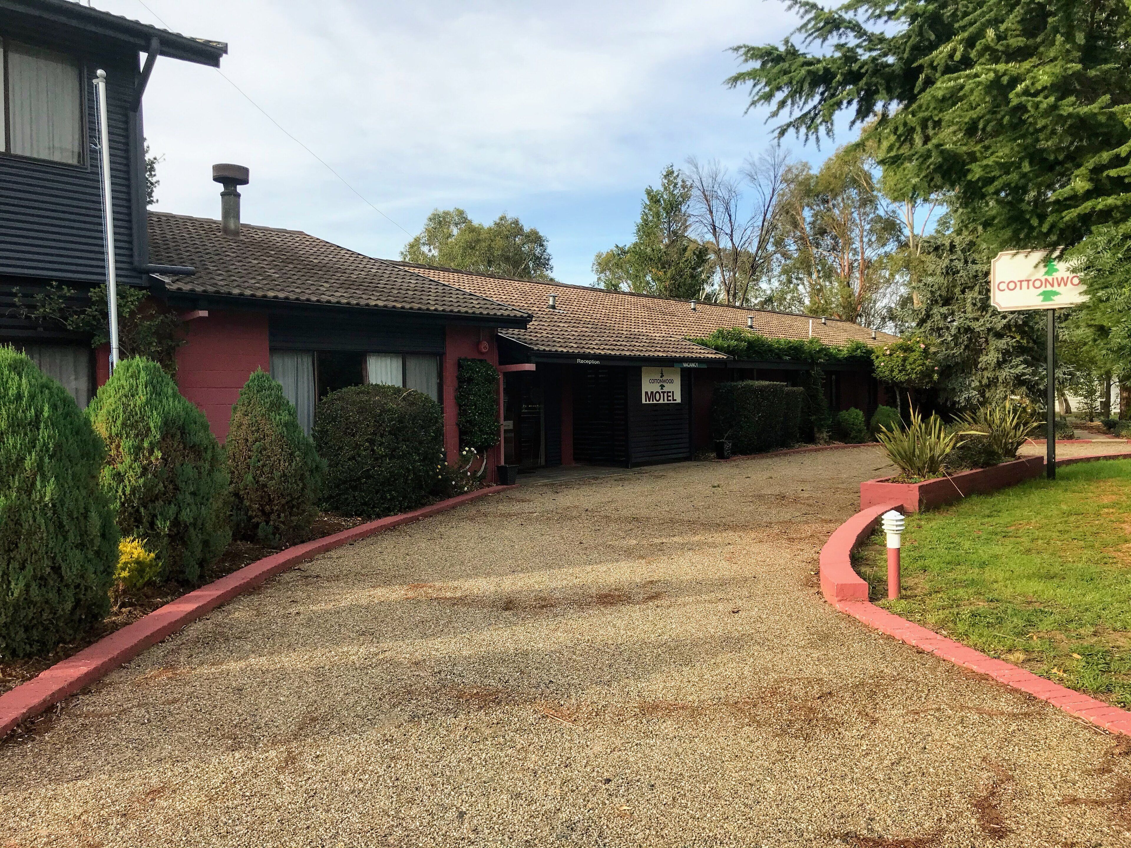 Un motel con camino de grava, una zona de recepción y un cartel con el nombre del motel.