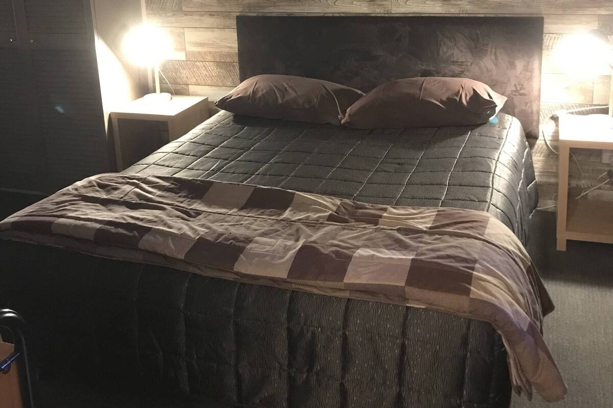 A bedroom with a bed, two bedside tables, a wall-mounted artwork, and a wooden wall panel.