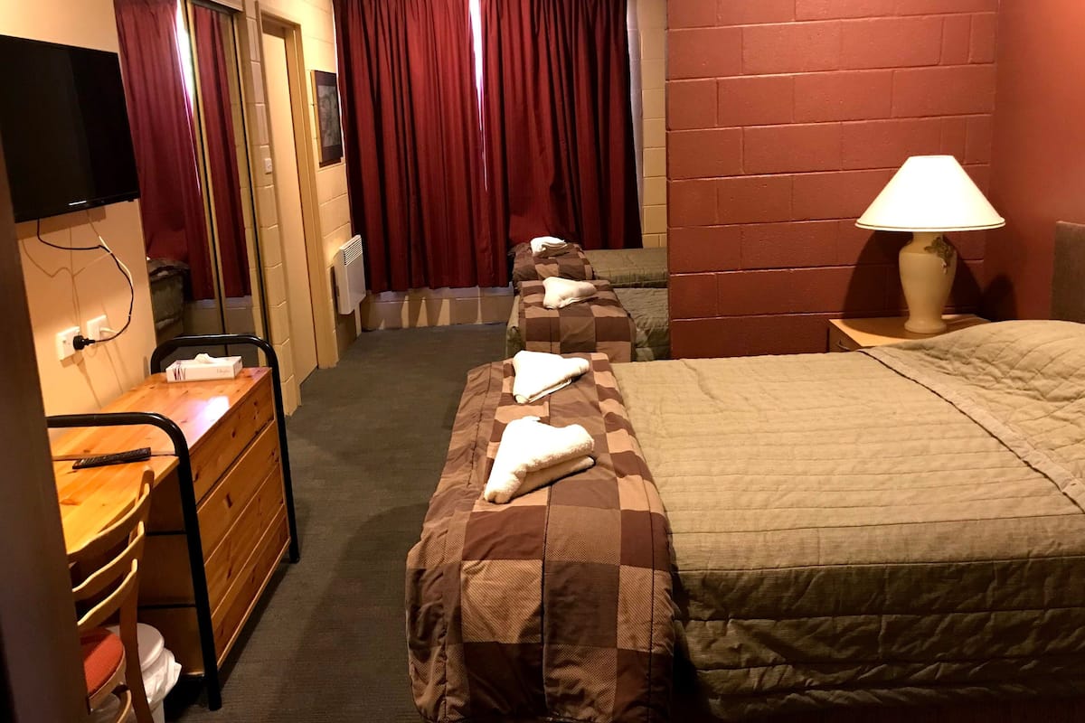 A hotel room with a bed, a desk with a chair, a lamp, and a TV mounted on the wall.