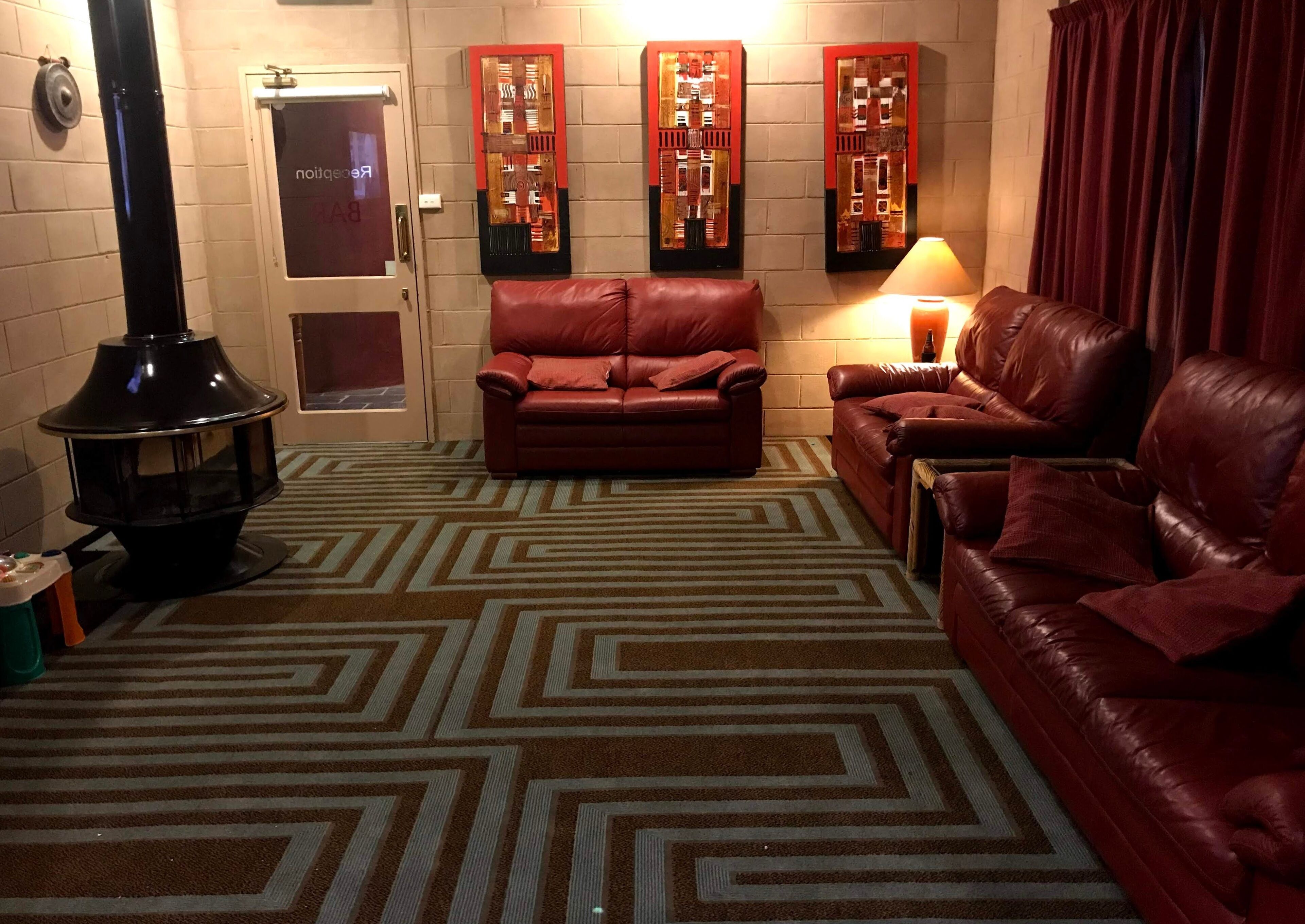 A cozy living room with a fireplace, leather sofas, patterned carpet, and decorative wall art.