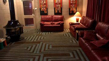 A cozy living room with a fireplace, leather sofas, patterned carpet, and decorative wall art.