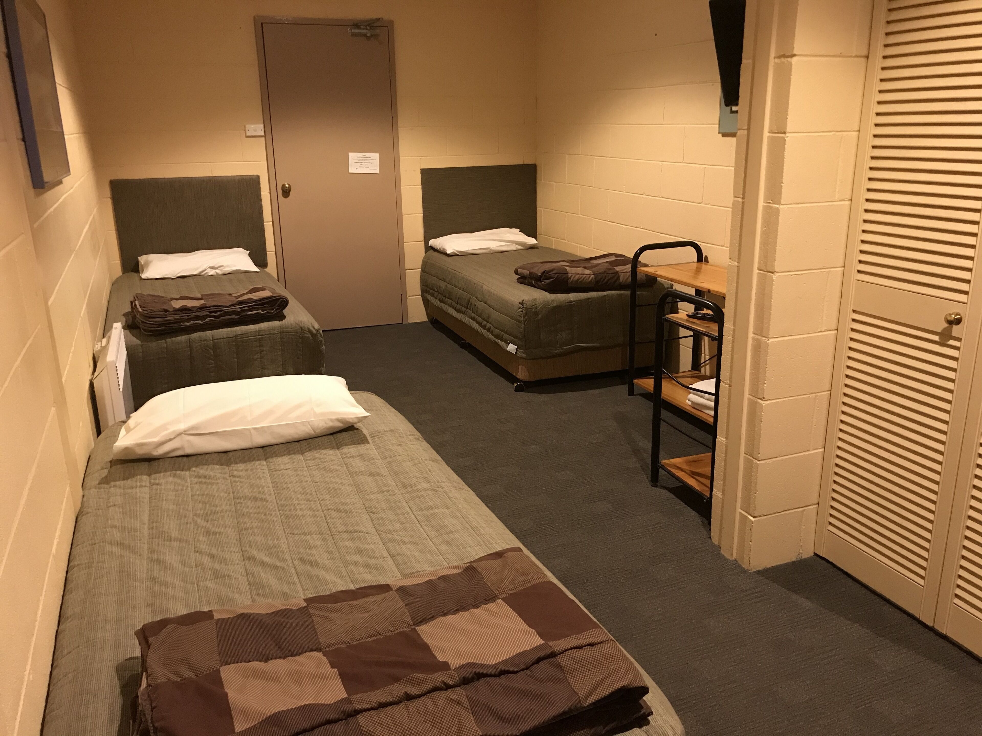 A narrow corridor with two single beds, a small table, and a wardrobe.