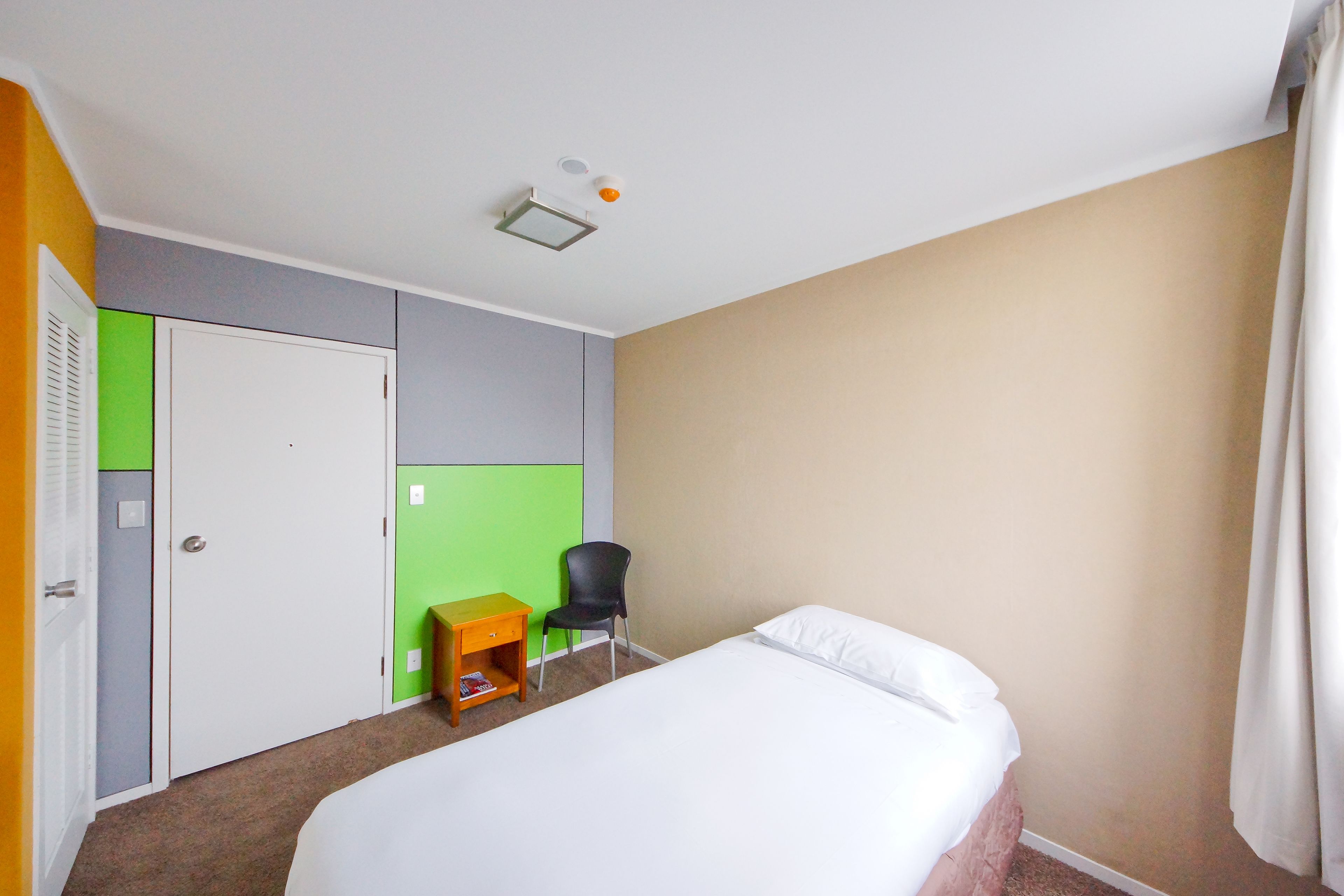 A hotel room with a bed, a desk, a chair, and a wardrobe.
