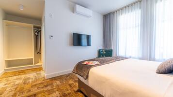 Habitación de hotel con cama, televisor montado en la pared, armario y ventana con cortinas.