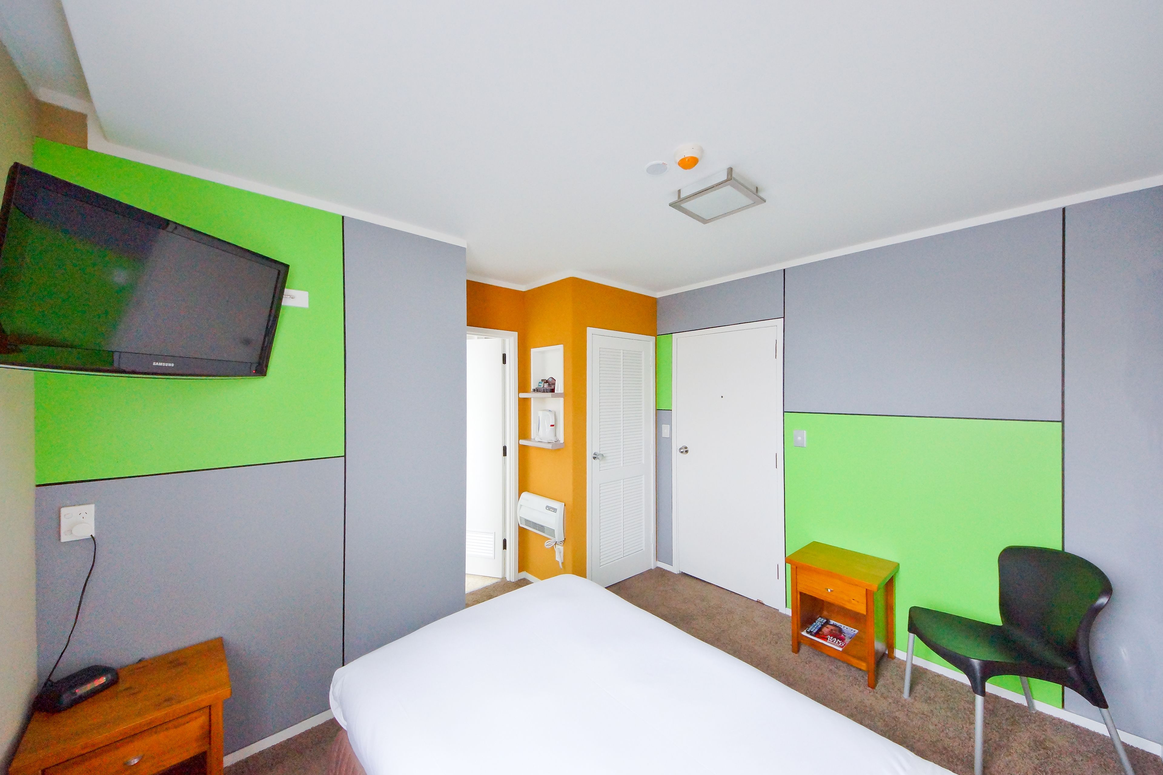 A room with a bed, a chair, a small table, a television, and a door.
