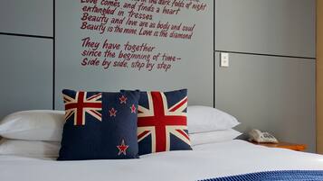 A neatly made bed with white linens and a blue blanket, a pillow with a Union Jack design, and a motivational quote on the wall.