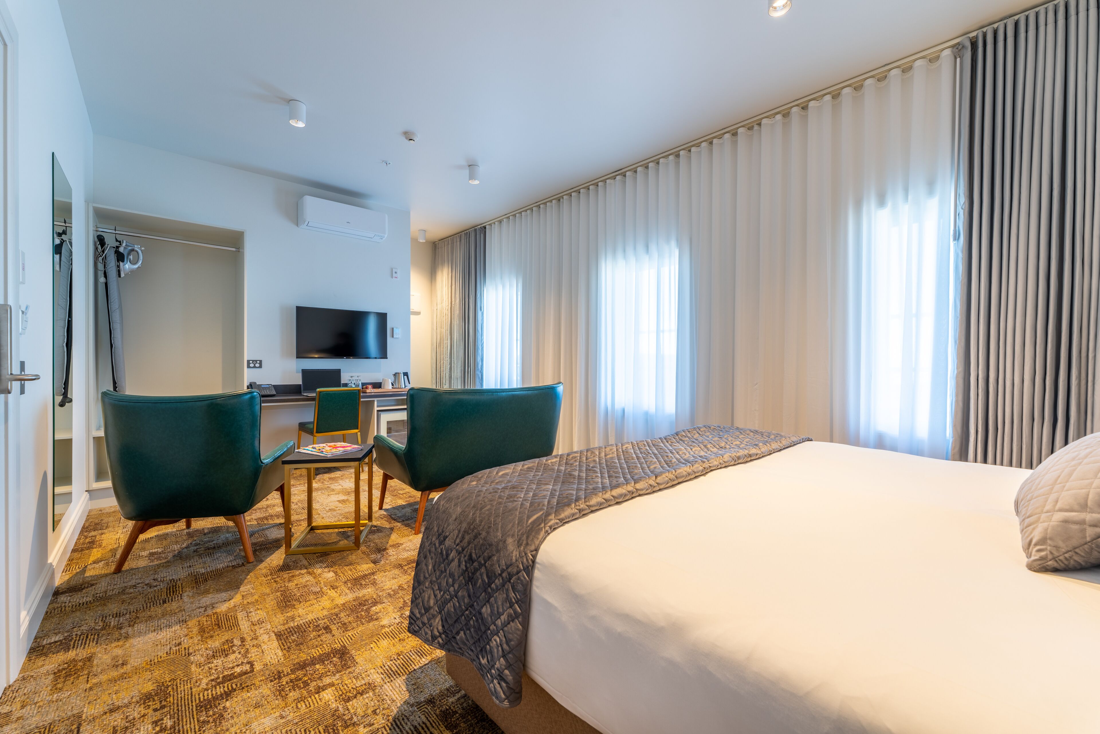 A hotel room with a large bed, a desk with a chair, a television, and a view of the city through the window.