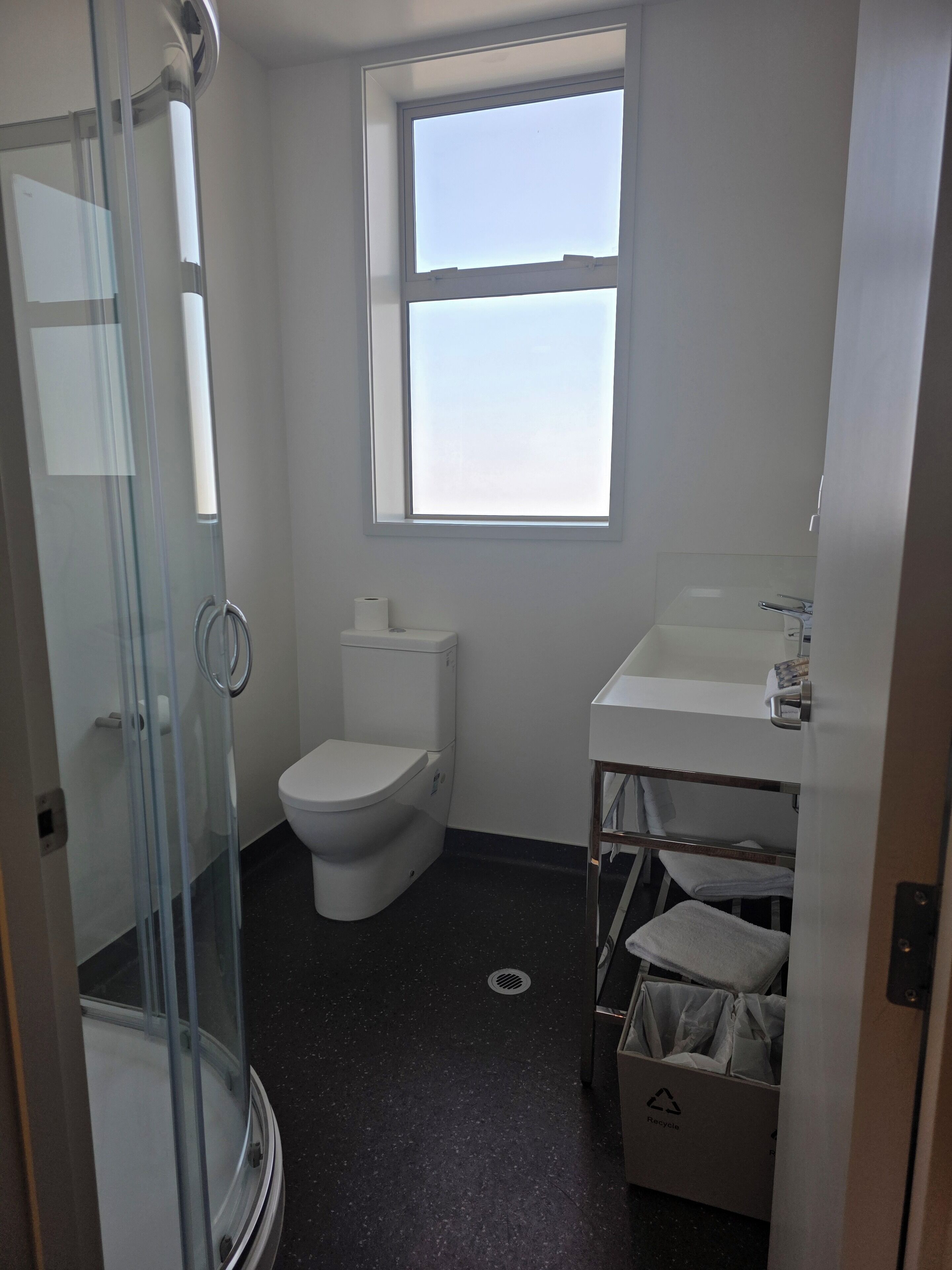 A bathroom with a glass shower enclosure, a toilet, a sink, and a window.
