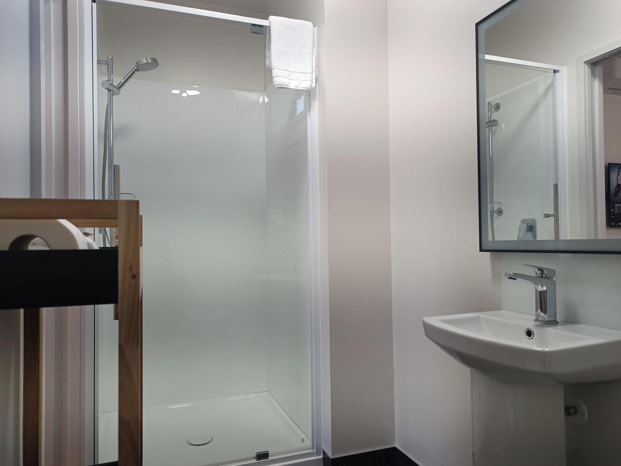 Un baño con ducha envuelta en vidrio, lavamanos y espejo.