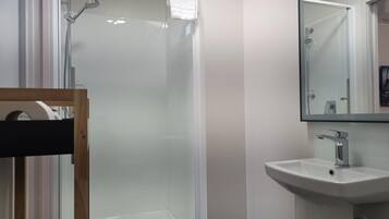 Un baño con ducha envuelta en vidrio, lavamanos y espejo.